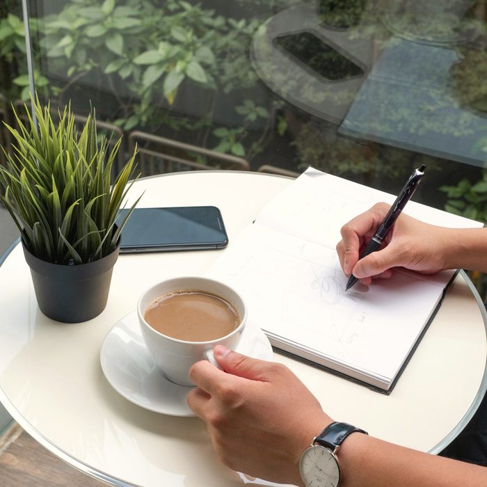 Manos escribiendo en una libreta junto a una taza de té y una planta